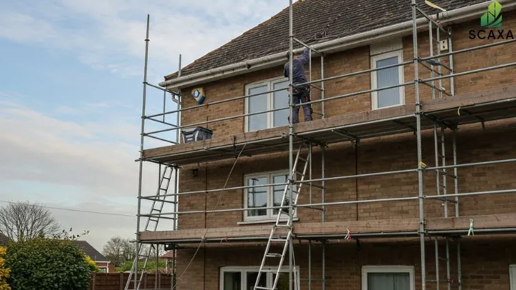 Worker on scaffolding performing maintenance on a residential building, showcasing SCAXA scaffolding solutions for construction and maintenance projects.