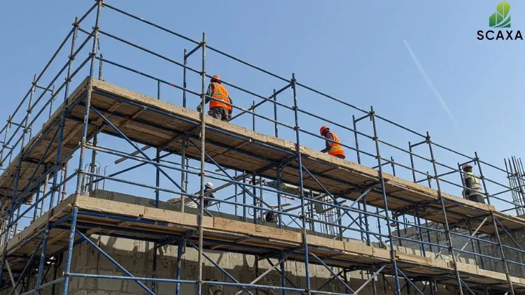 Construction workers on scaffolding structure, wearing safety gear, engaged in building activities, with SCAXA logo in the corner, illustrating scaffolding services in construction projects.