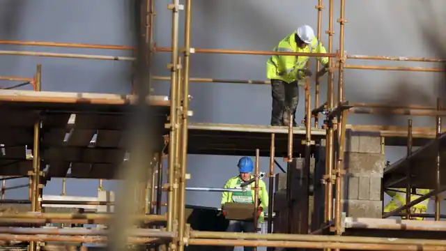 Workers in hi-vis vests maintaining scaffolding on a construction site